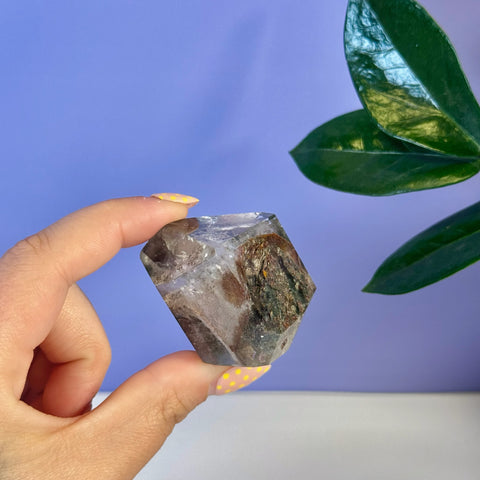 Hand holding a clear Garden Quartz free form with earthy brown and green inclusions.