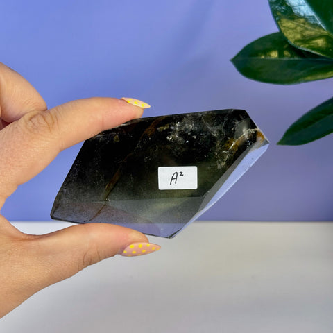 Dark green garden quartz free form crystal, held by fingers with yellow polka dot nails.