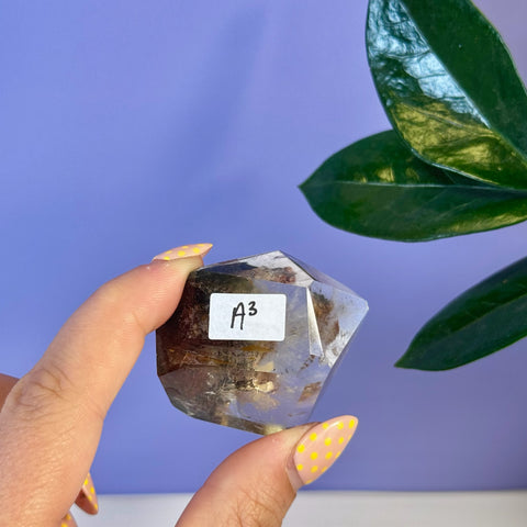 Hand holding a translucent Garden Quartz Free Form crystal, showing earthy inclusions and a polished, faceted shape.
