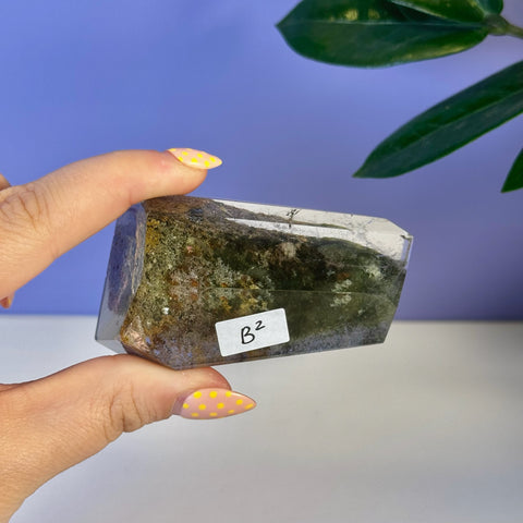Garden Quartz Free Form, clear with dark green and brown inclusions, held by hand.