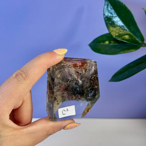 Clear garden quartz free form with dark red, black, and green mineral inclusions.