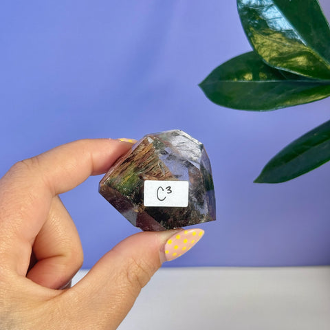 Garden Quartz free form, C3 variant, held in hand, showing natural inclusions and facets.