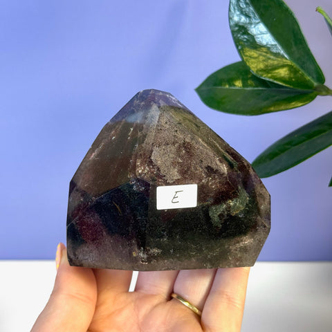 Dark, faceted Garden Quartz free form with internal inclusions, held in a hand.