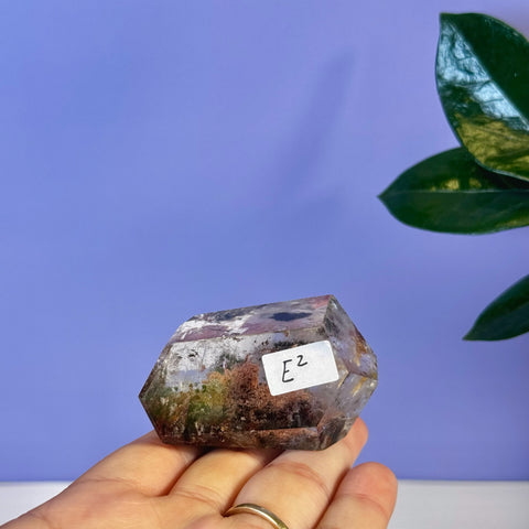 Garden Quartz Free Form, clear crystal with green and reddish-brown inclusions, held in hand.