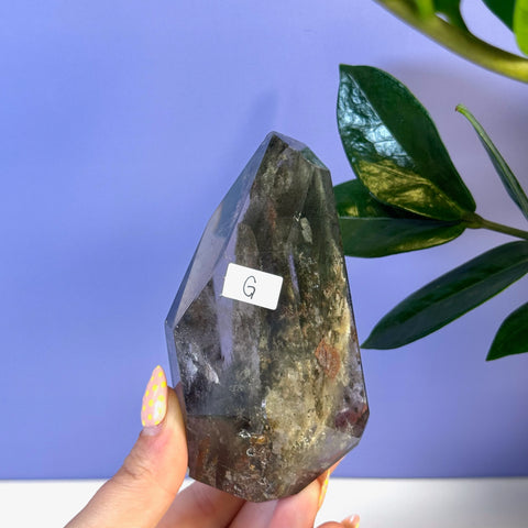 Dark Garden Quartz free form crystal with natural inclusions, held against a purple background.