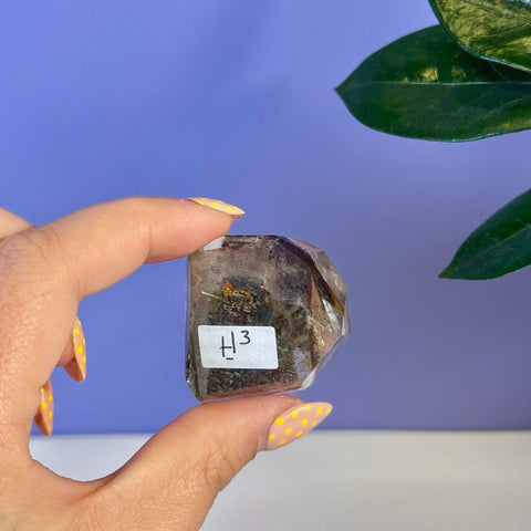 Clear Garden Quartz free form (H3) with dark inclusions, held by fingers with yellow polka dot nails.
