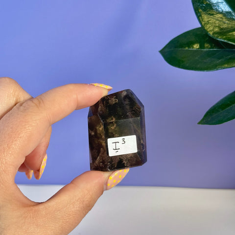 Dark brown Garden Quartz free form crystal, held by hand, with "I3" label.