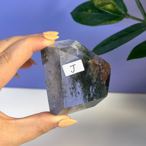 Garden Quartz free form, clear with dark green inclusions, held by hand.