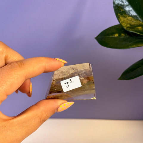 Hand holding a small, clear Garden Quartz Free Form (J3) with natural brown and green inclusions.