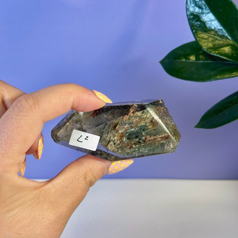 Hand holding L2 Garden Quartz Free Form, a clear crystal with green and reddish inclusions.