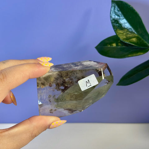 Clear garden quartz free form with green and reddish inclusions, held by a hand with yellow polka dot nails.