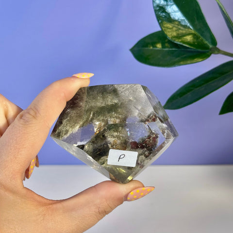 Garden Quartz free form, clear with green and reddish inclusions, held by hand.