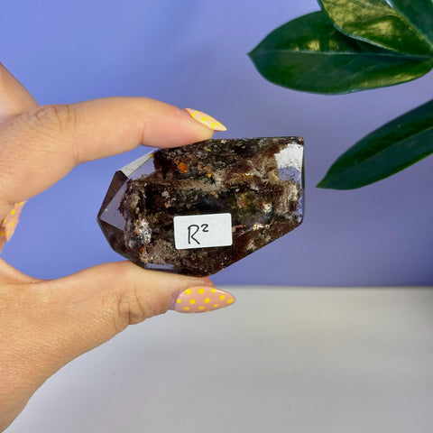 Dark brown garden quartz free form crystal with earthy inclusions, held by a hand with yellow polka dot nails.