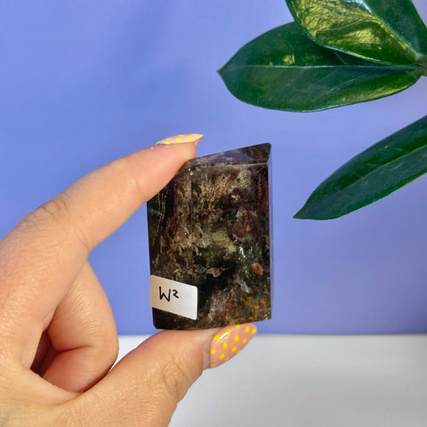 Dark brown and green Garden Quartz free form crystal, held by a hand with yellow polka dot nails.