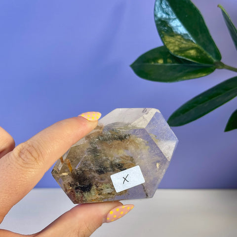 Hexagonal Garden Quartz free form, clear with dark green and brown inclusions, held by fingers.