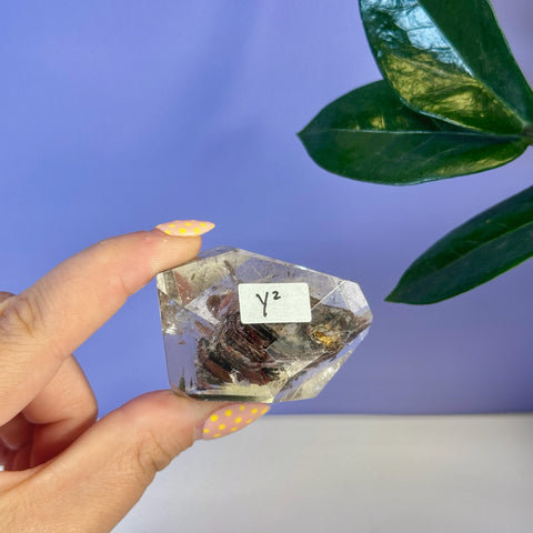 Clear Garden Quartz free form crystal with dark red and gold inclusions, held by fingers with yellow polka dot nails.