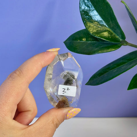 Clear Garden Quartz free form crystal with dark green inclusions, held by fingers with yellow polka dot nails.