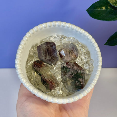 Four dark green and purple Garden Quartz Gusher crystals in a white bowl with clear chips.