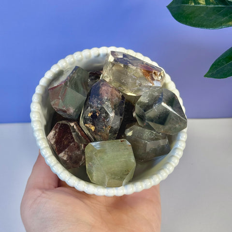 A white fluted bowl filled with various Garden Quartz Gusher crystals in shades of green, brown, and clear.