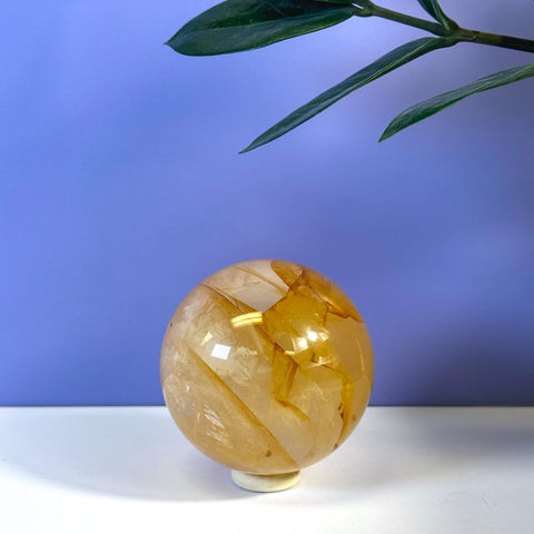 Girasol Golden Healer Sphere with warm amber tones and internal fractures on a white stand.