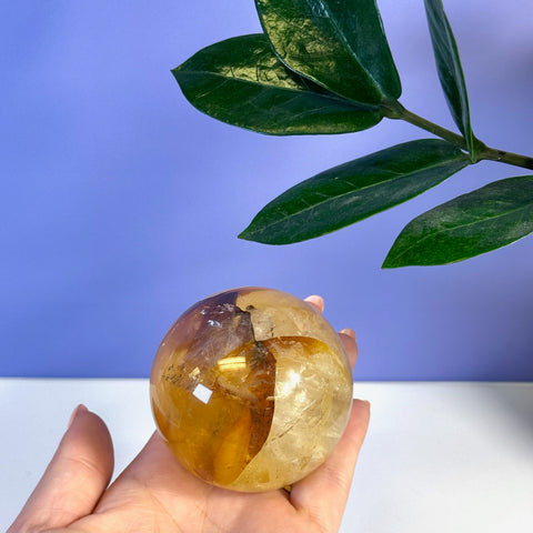 Hand holding a polished Girasol Golden Healer Sphere with warm yellow and orange tones.