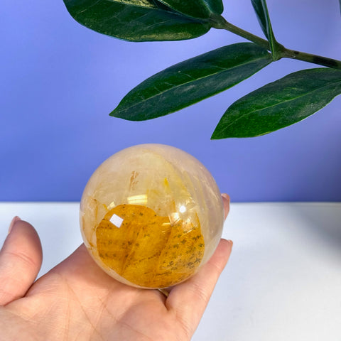 Hand holding a polished Girasol Golden Healer sphere with warm yellow and clear tones.
