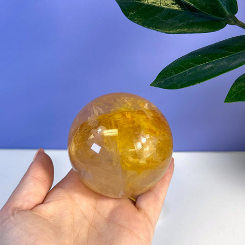 Hand holding a translucent Girasol Golden Healer sphere with warm yellow and orange hues.