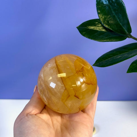 Hand holding a polished Girasol Golden Healer sphere with warm yellow and orange inclusions.