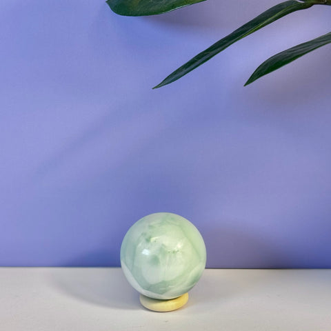 Smooth green alabaster sphere with white swirls on a light stand against a purple background.
