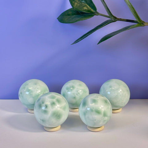 Five small, polished green alabaster spheres with white marbling on light stands.