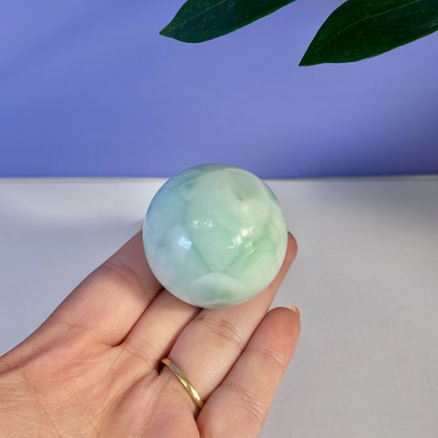 Hand holding a smooth, polished green alabaster sphere with white marbling.