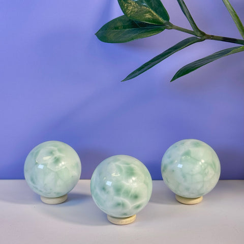 Three polished green alabaster spheres with white marbling on light wood stands.