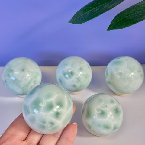 Hand holding a smooth, polished green alabaster sphere with four more spheres on a white surface.