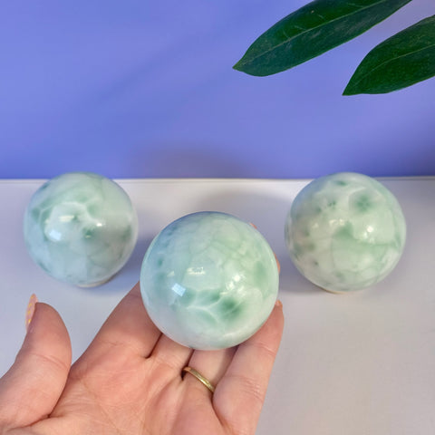 Hand holding a smooth, polished green alabaster sphere with two more in the background.