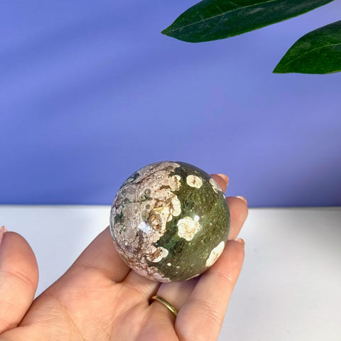 Polished green cherry blossom sphere with white and brown floral patterns, held in a hand.
