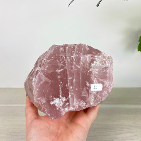 Large, translucent rose quartz chunk with a soft pink hue and natural crystalline texture held in a hand.