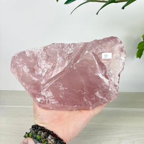 Large, translucent rose quartz chunk with a natural crystalline texture held in a hand against a white background.