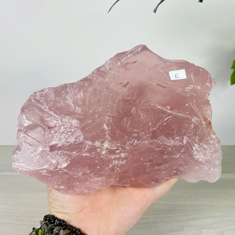 Large, translucent rose quartz chunk with a natural, raw texture held in a hand against a neutral background.