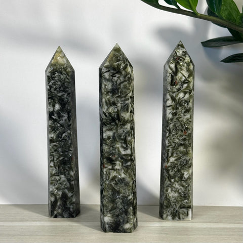 Three tall, pointed green mica crystal towers with dark inclusions on a white surface.