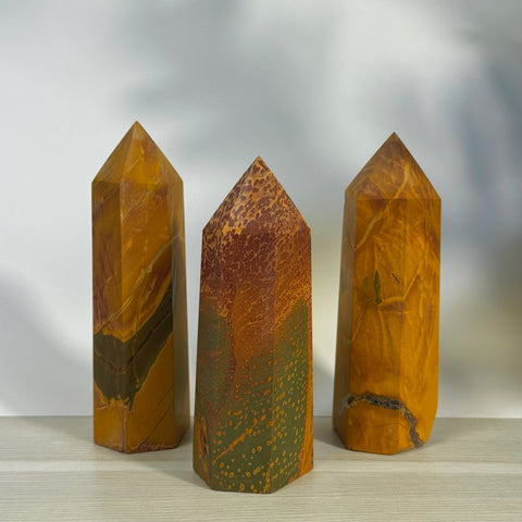 Three imperfect realgar towers with pointed tops, featuring earthy orange, red, and green tones.