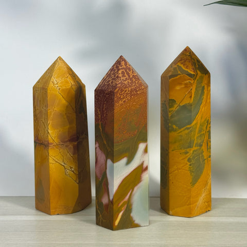 Three polished realgar crystal towers in varying shades of orange, brown, and green.