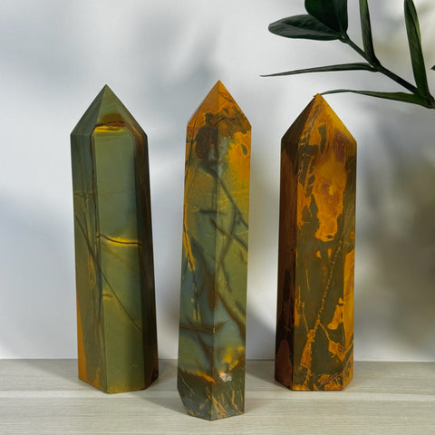 Three polished realgar crystal towers in varying shades of green, brown, and orange, with natural striations.