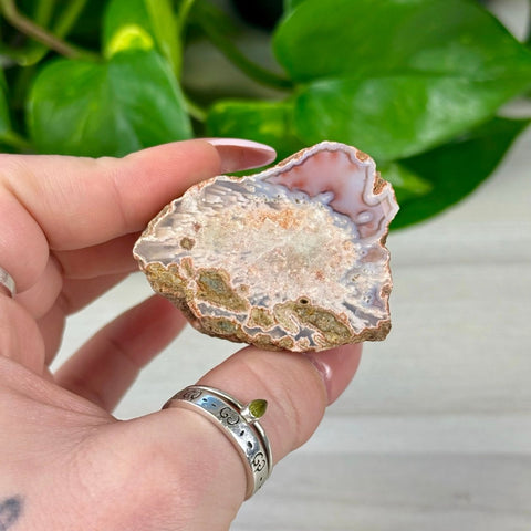 Pink, white, and brown individual agate slice held in hand, showing natural crystal formations.