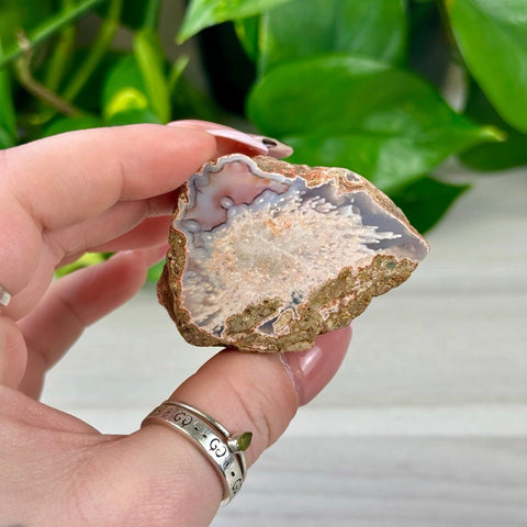 Hand holding a small, rough-cut individual agate with white, pink, and grey banding.