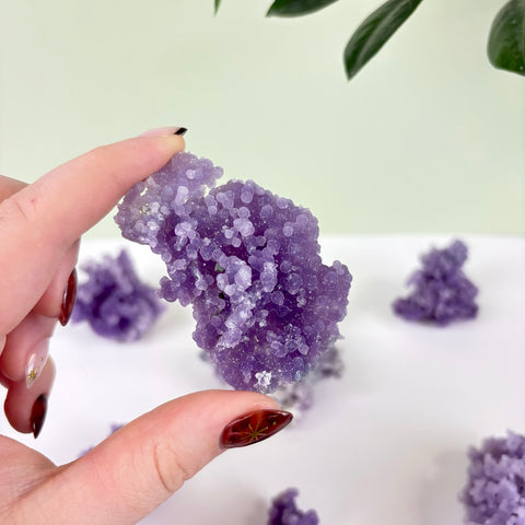 Hand holding a cluster of deep purple grape agate with sparkling, spherical crystal formations.