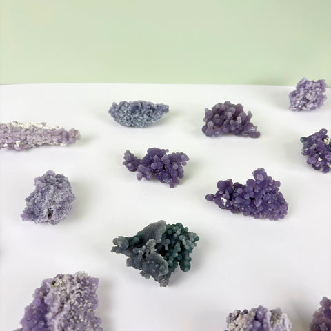 Assorted grape agate clusters featuring small, spherical purple crystals arranged on a white surface.