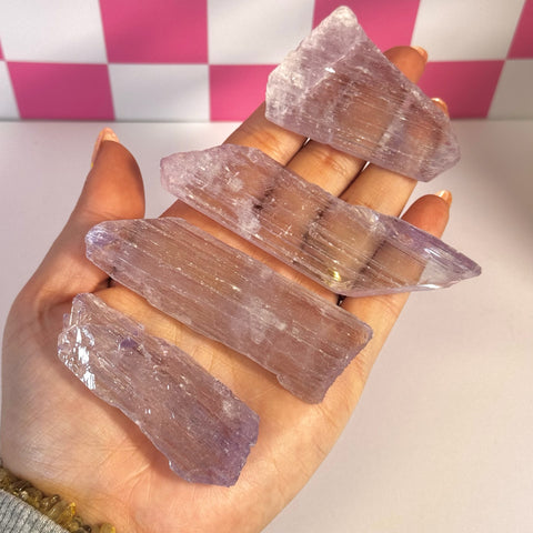 Hand holding five raw, elongated kunzite crystals with a pale lavender hue.
