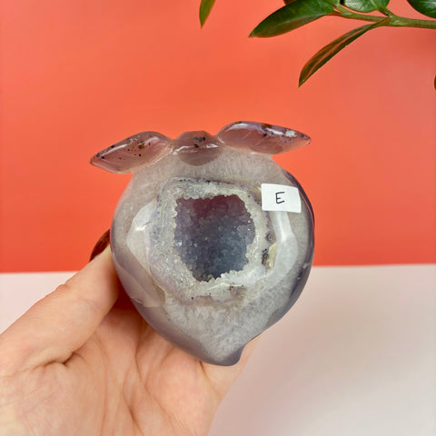 Peach-shaped druzy agate crystal carving with a sparkling purple geode center held in a hand.