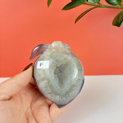 Handheld peach-shaped druzy agate carving featuring a sparkling crystal geode center and smooth purple stone edges.