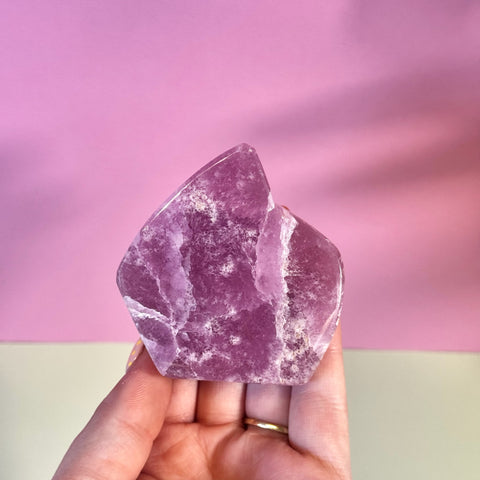 Juicy pink aragonite free form with wave-like patterning, held in a hand.